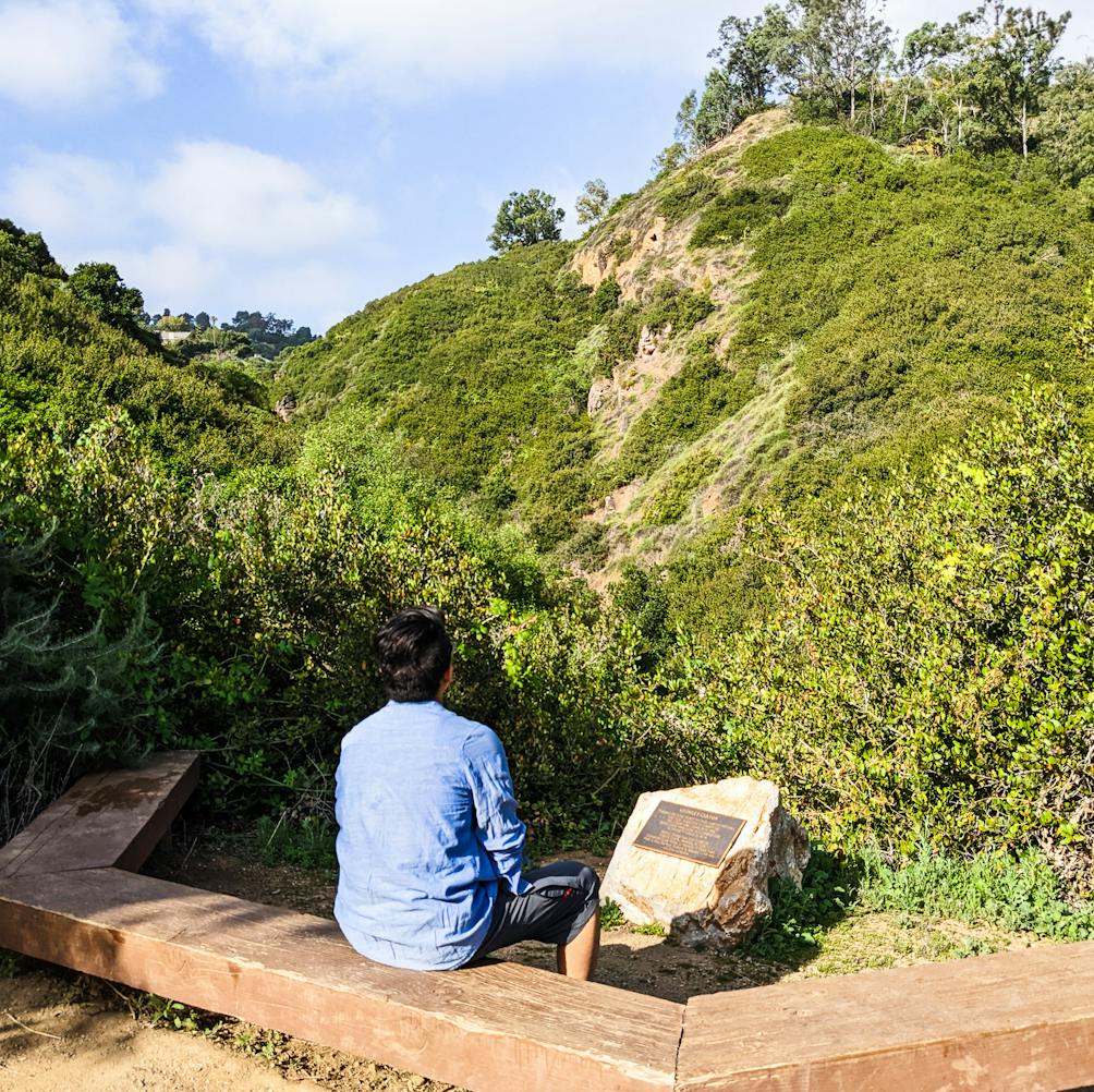 Hiker at a bench reading a placard sign in George F Canyon Preserve in Ranchos Palos Verdes 