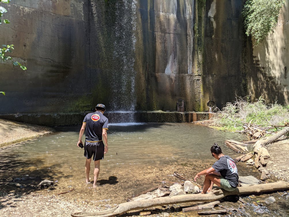 Two men wading into the water basin of historic Brown Mountain Dam in Southern California 