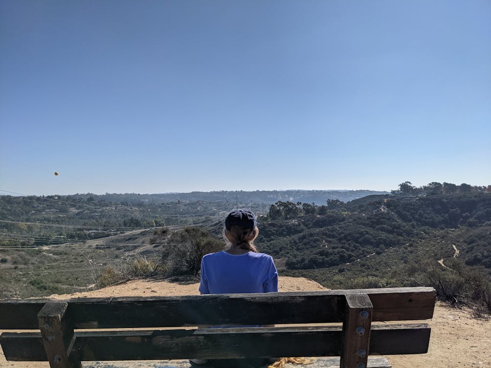 A woman sits at a bench overlooking vast green scenery at Manchester Preserve in San Diego County 