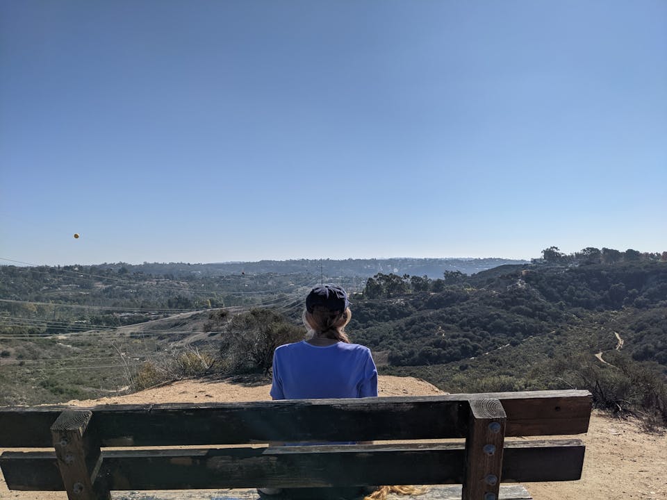 A woman sits at a bench overlooking vast green scenery at Manchester Preserve in San Diego County 