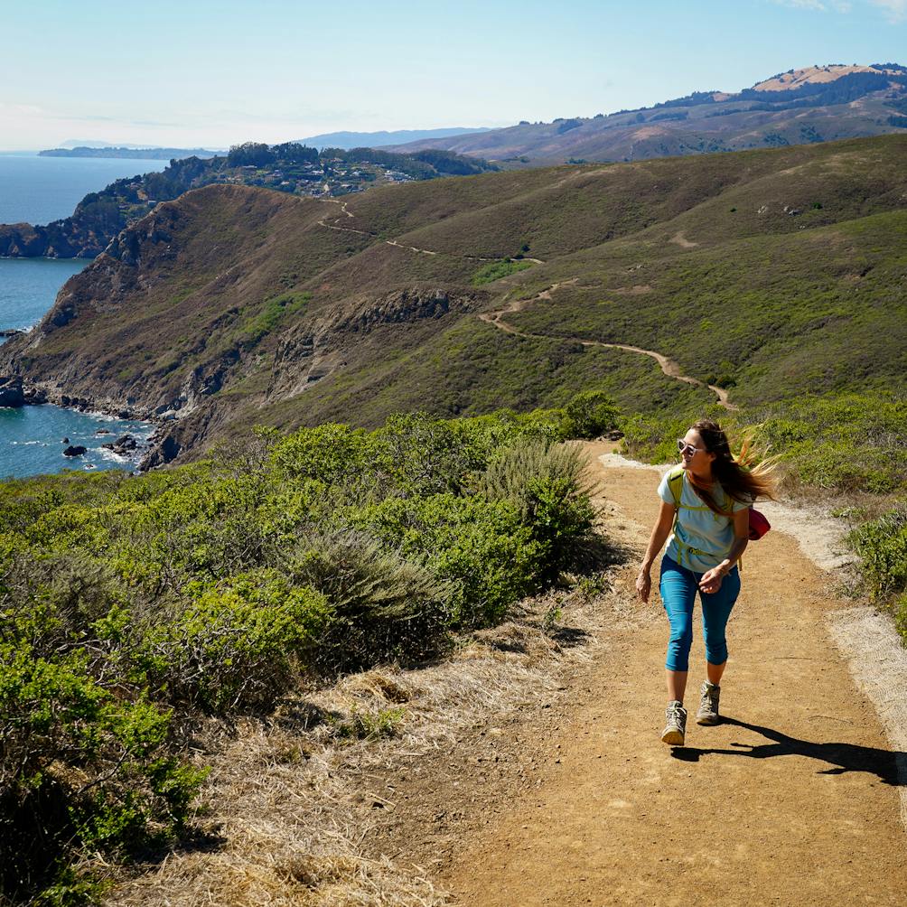 Woman hiking up the Coastal Trail next to the ocean in the Marin Headlands 