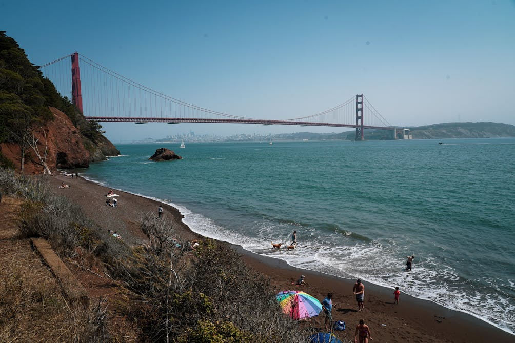 Kirby cove beach with a colorful sun umbrella and people on the beach with the Golden Gate Bridge in the background