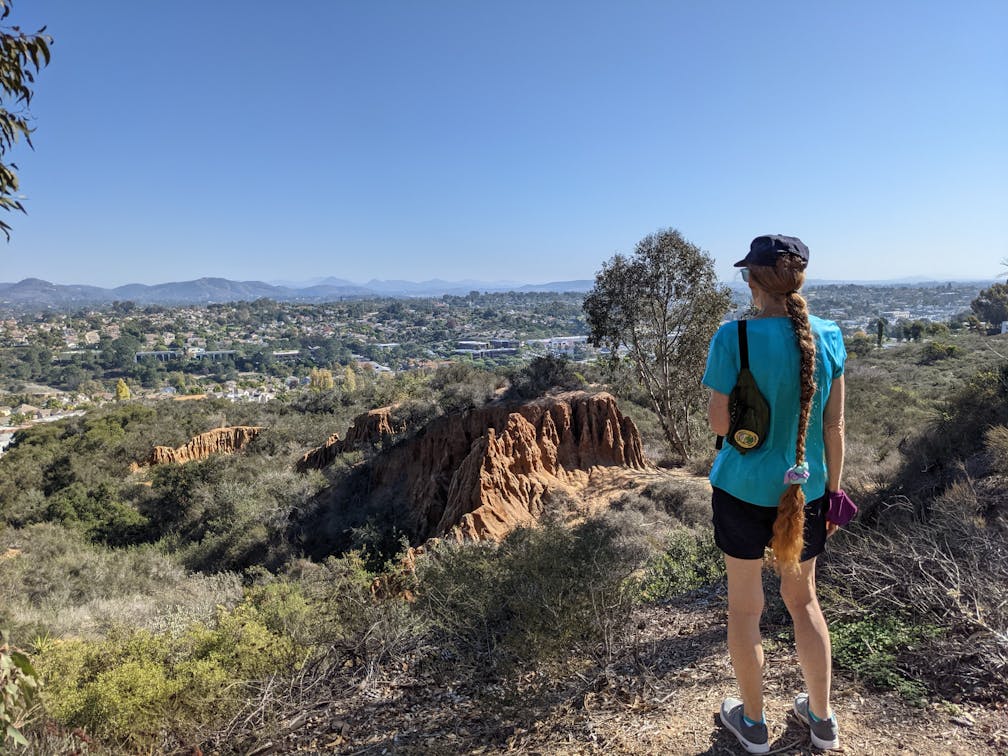 A hiker surveys the sandstone formation and distant mountain views at Encinitas Ranch in North San Diego County