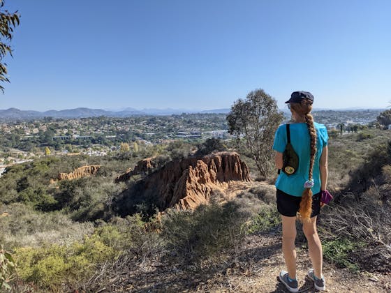 A hiker surveys the sandstone formation and distant mountain views at Encinitas Ranch in North San Diego County