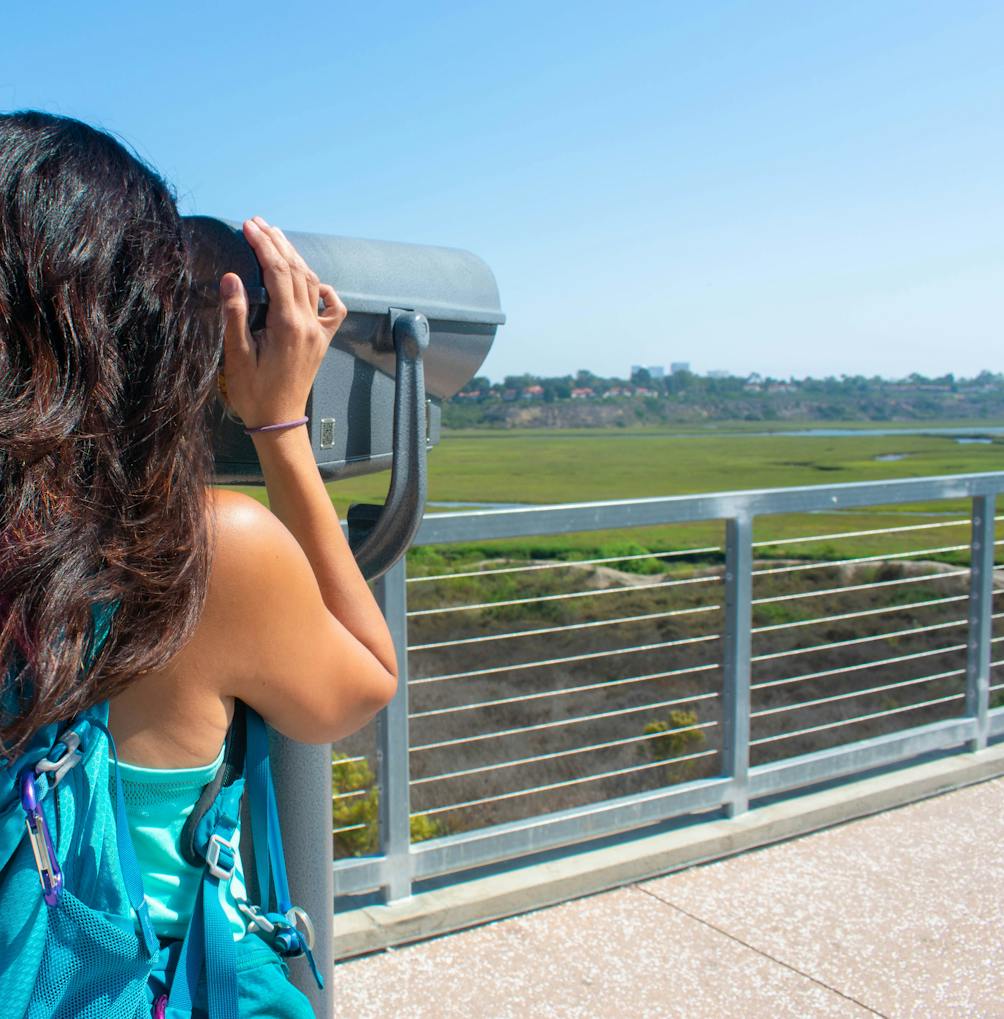 A woman looks through a telescope out towards Upper Newport Bay Nature Preserve in Orange County 