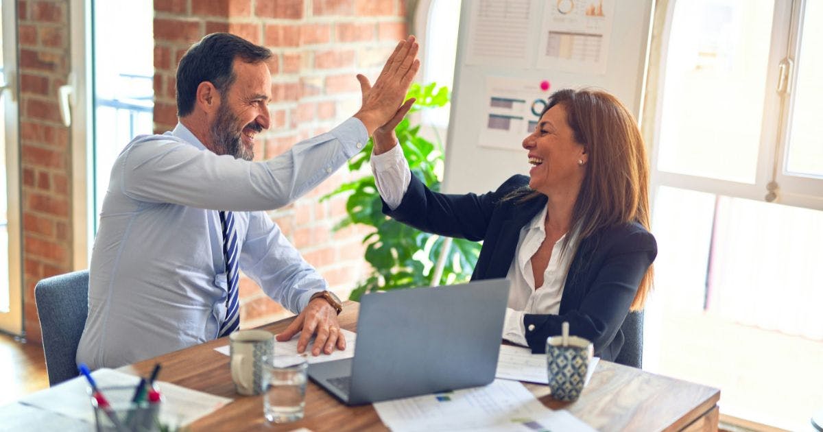 Two colleagues high-fiving, symbolising teamwork and success achieved with spend management software.