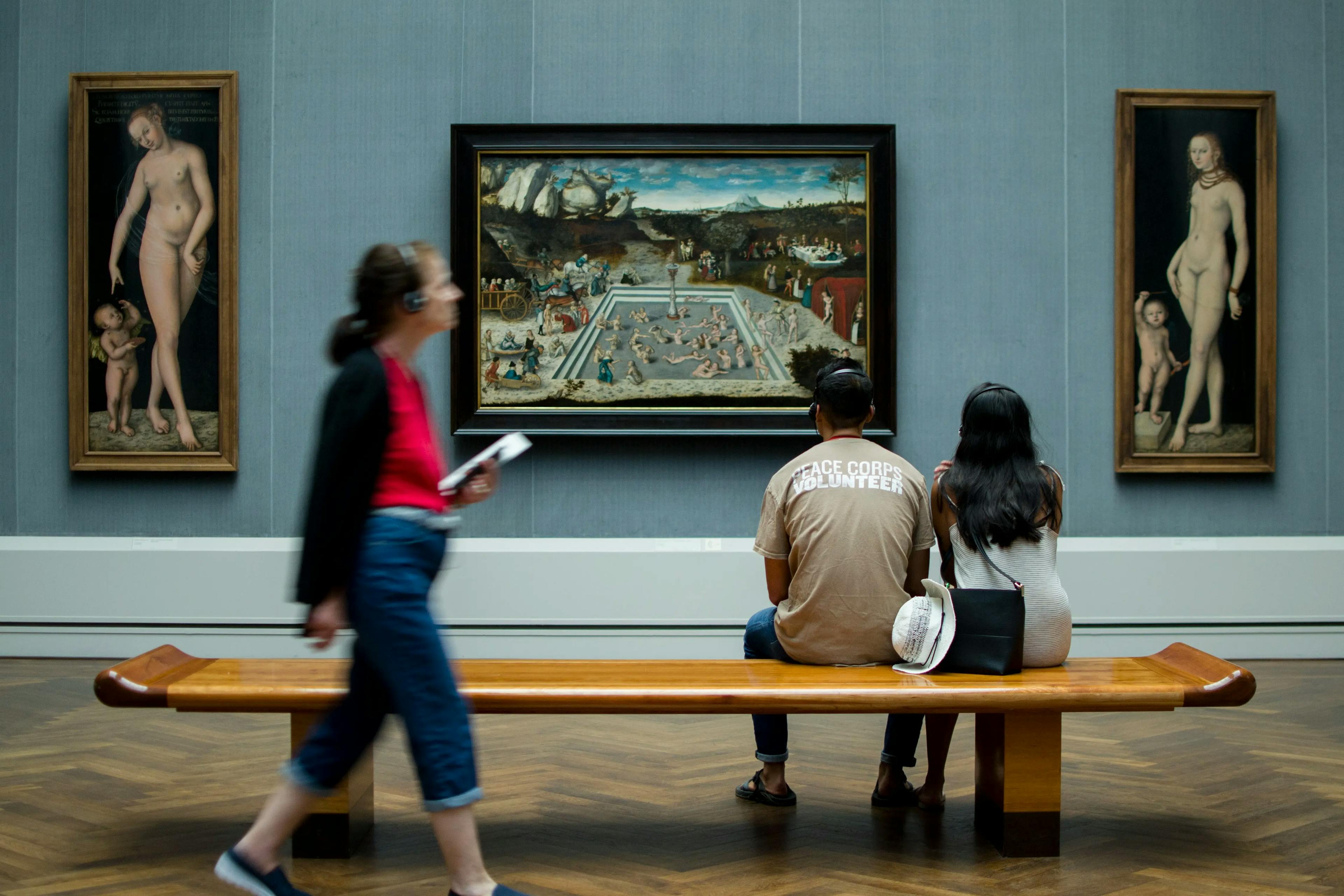 Visitatori osservano un dipinto mentre una signora attraversa la stanza ascoltando un'audioguida