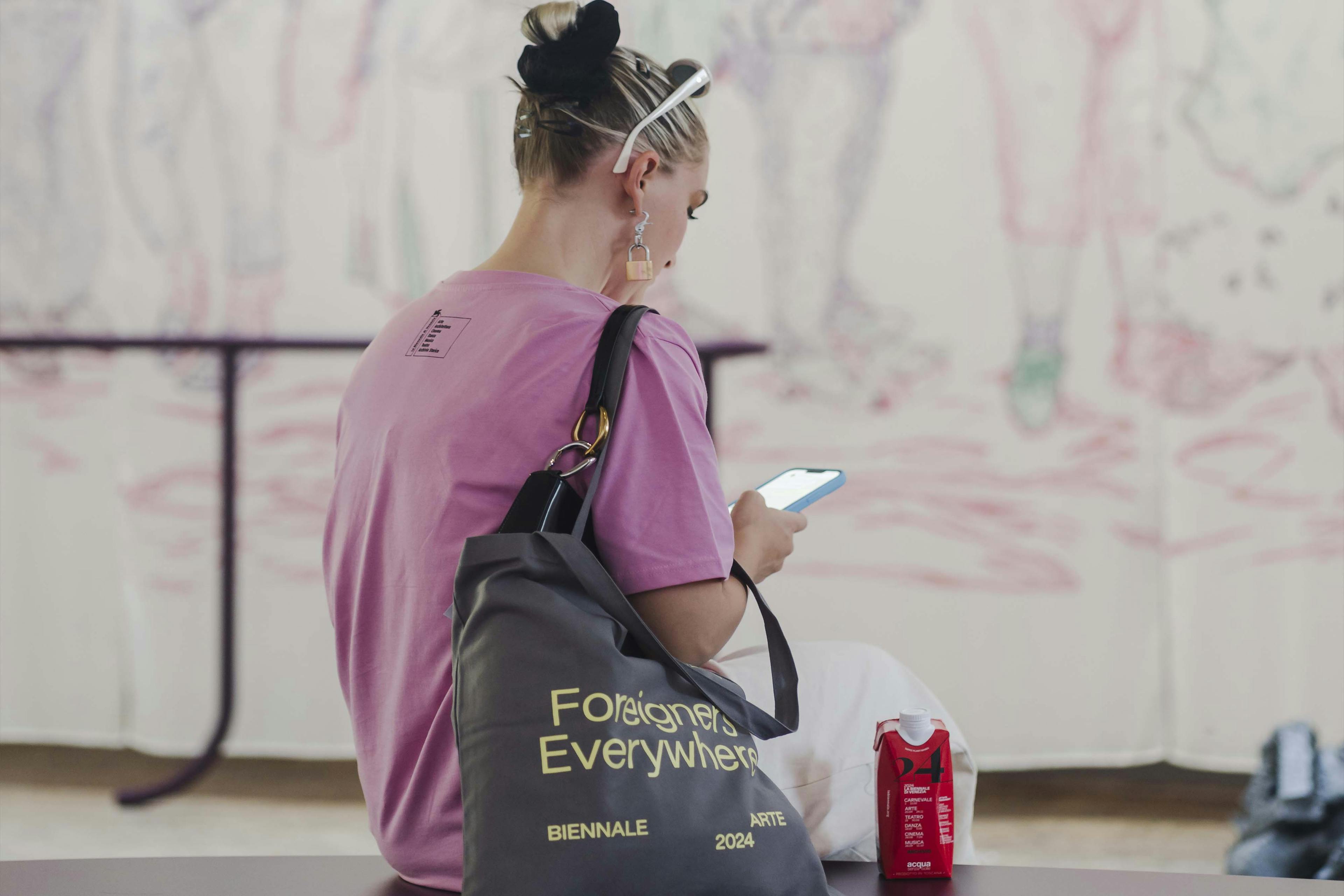 Girl at the Biennale Arte 2024 takes a break by sitting down and checking her phone
