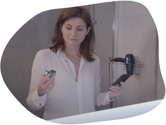 Mujer en el baño, mirando su puff en una de sus manos, y sosteniendo su celular en la otra.