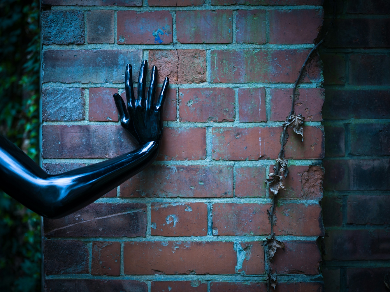 Photograph of a brick wall with the human form of a shiny black hand and arm pressed up against it.