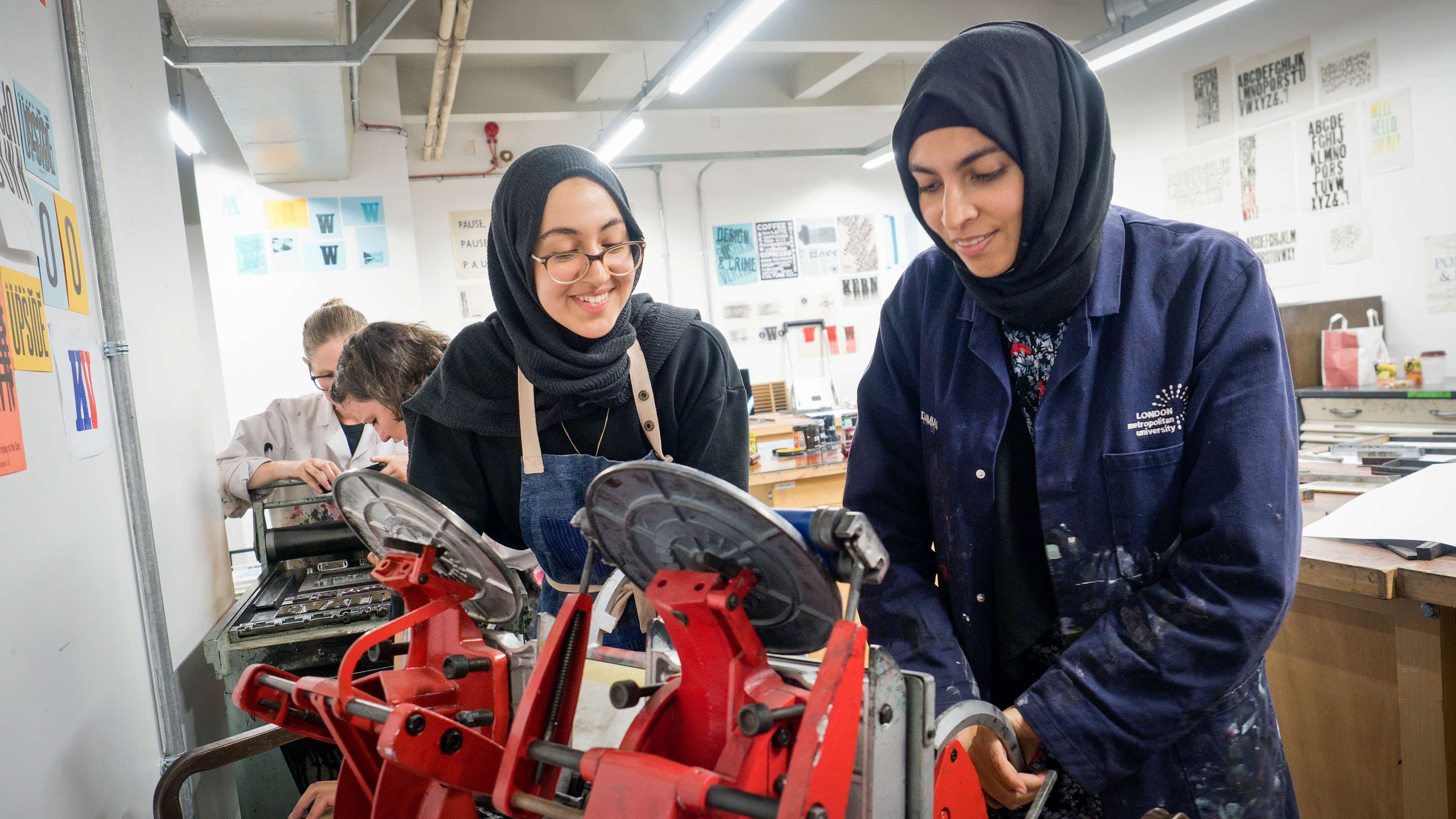 Photograph showing two printmakers operating a printing press at London Metropolitan University.