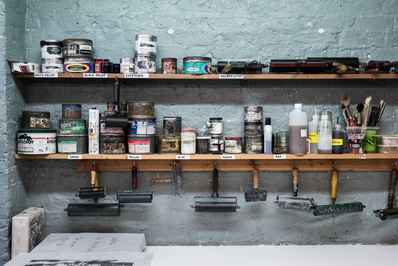Photograph of shelves in a printmaking studio containing paints, rollers and brushes.