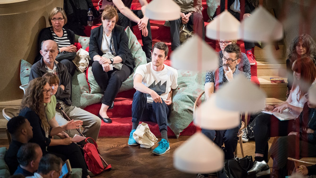 Photograph of a discussion taking place in the Readng Room at Wellcome Collection, showing people sitting on the carpeted staircase and chairs.