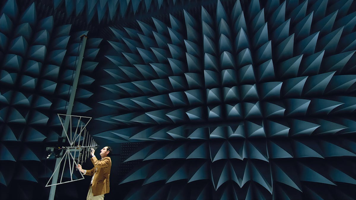 Colour photograph of a man adjusting an aerial in a soundproof chamber with lots of blue points sticking out from the walls.