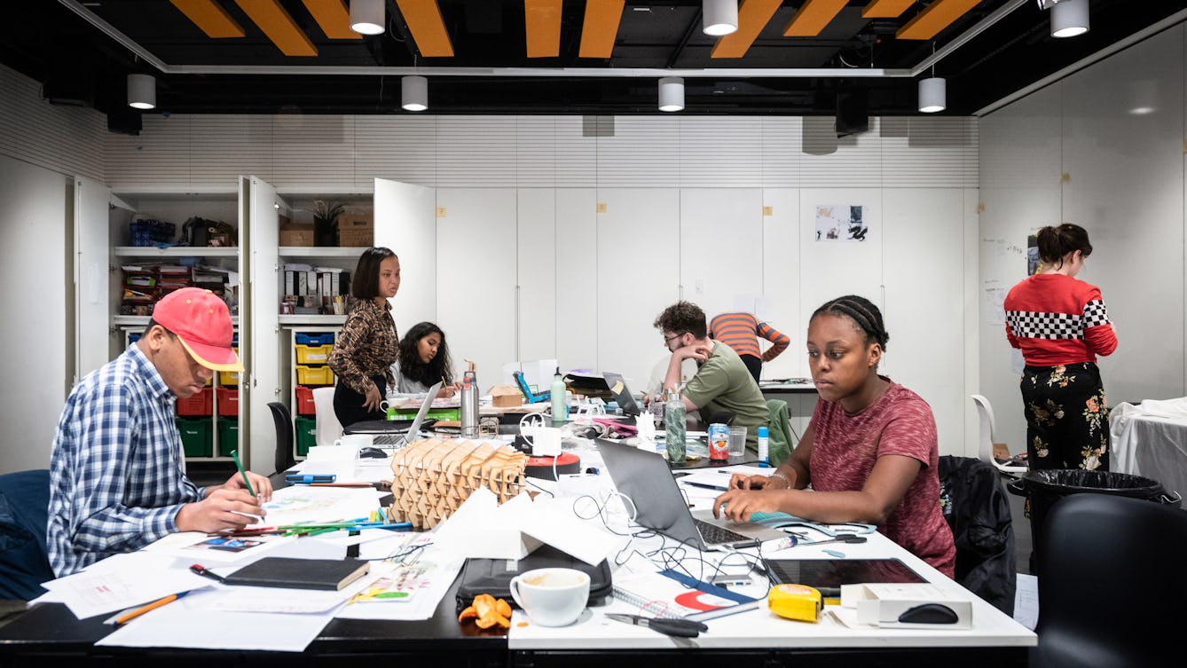 Photograph of the studio space at Wellcome Collection showing a group of young people working at a central table, which is covered in drawing and design material.