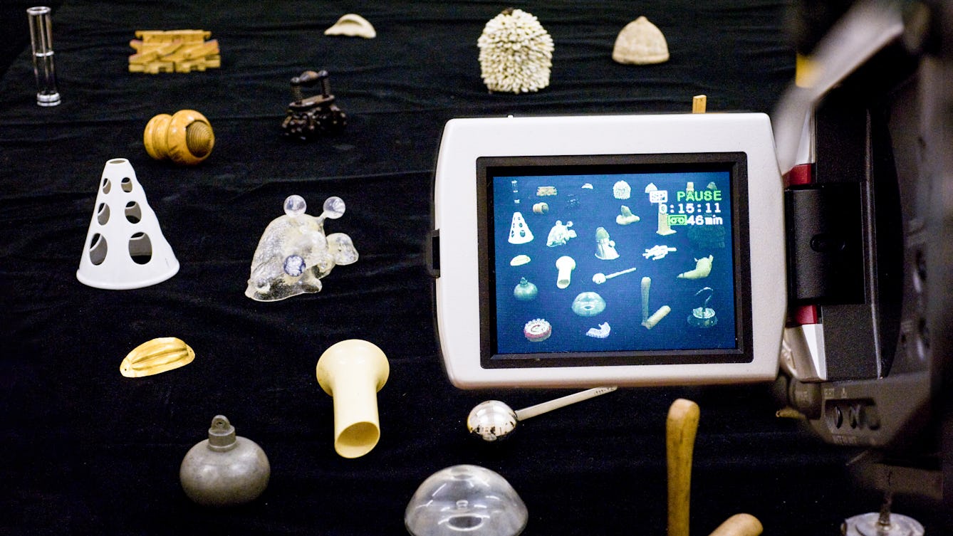 Photograph of a video camera screen showing a view of a table with several objects laid out on a. black background.