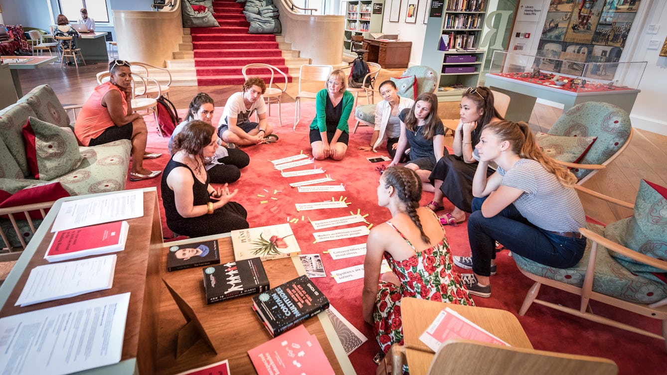 Photograph of a group of people sitting in a circle on the carpet in the Wellcome Collection Reading Room, engaged in discussion.