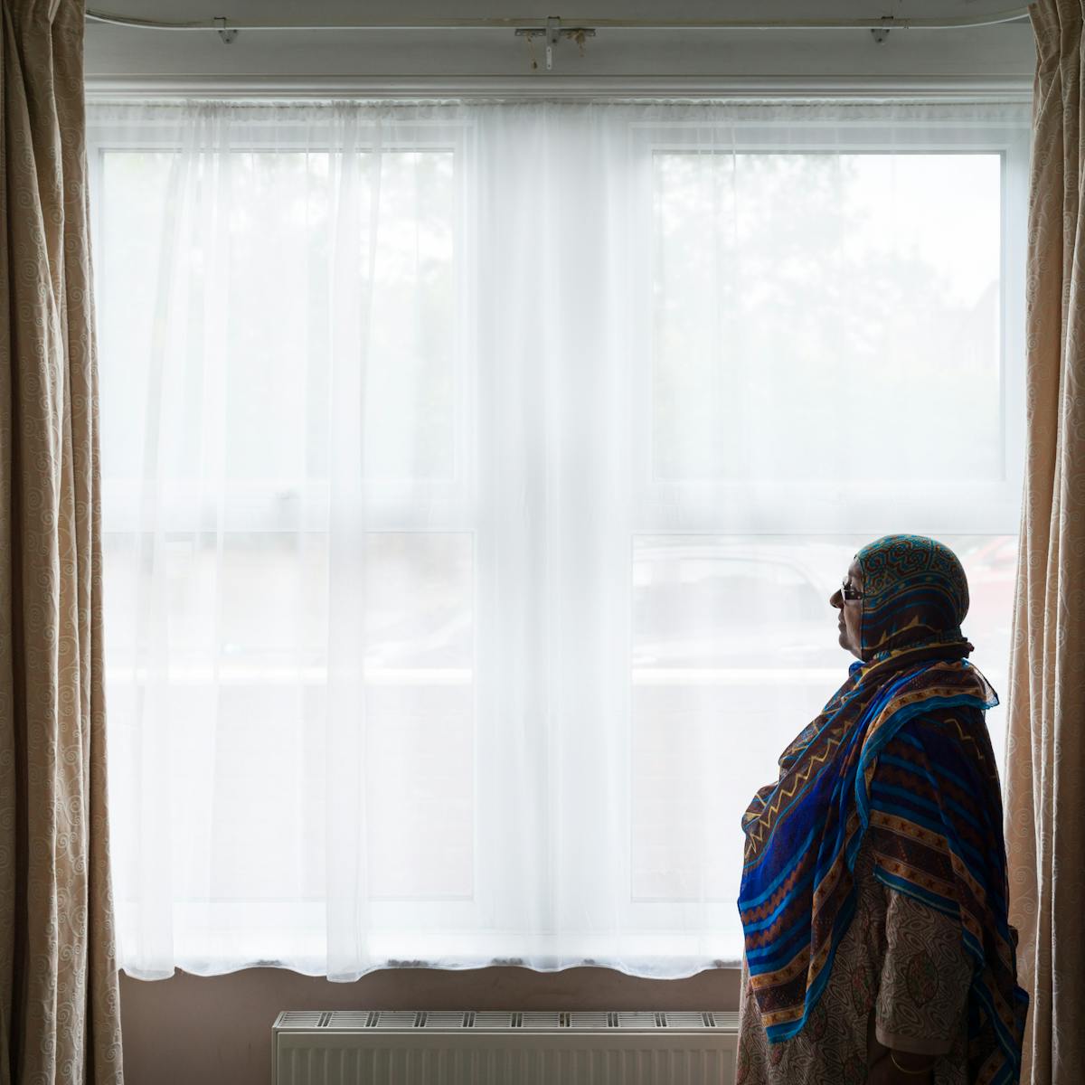 Photograph of a woman standing by the front windows in her living room.