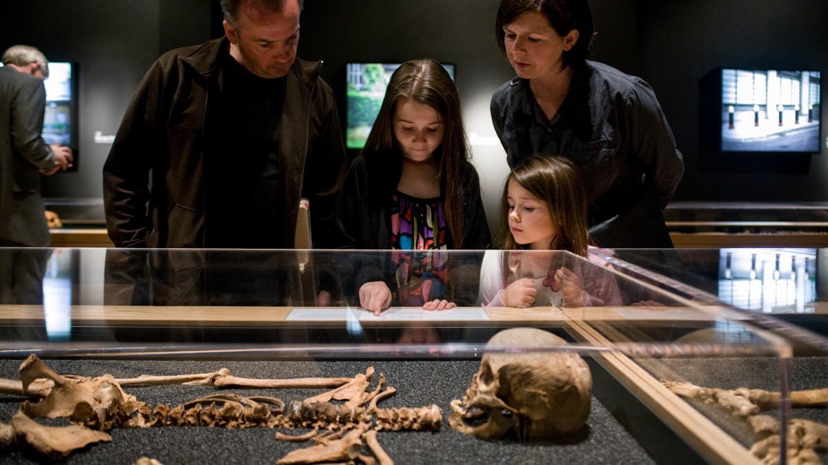 Photograph of a family looking at a display case showing one of the skeletons that formed part of the Skeletons: London’s Buried Bones exhibition at Wellcome Collection.