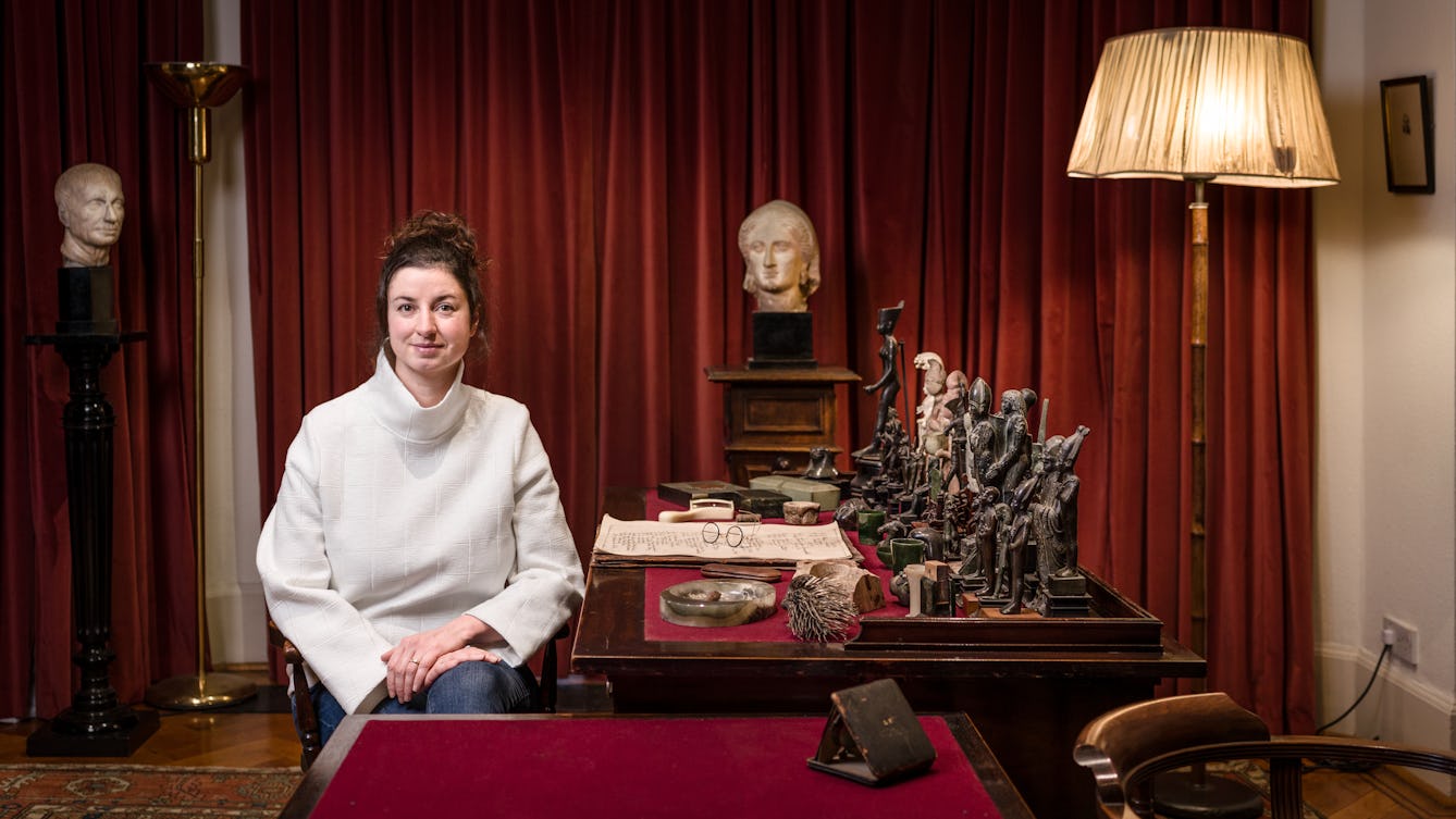 Photographic portrait of artist Emma Smith sitting at Freud's desk in the Freud Museum, London.