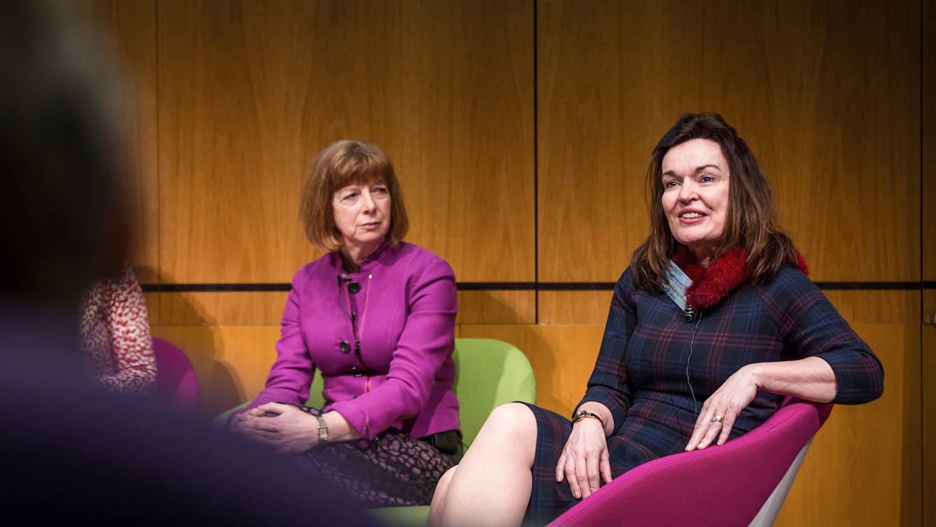 Photograph of two women taking part in a panel discussion seated on a stage in an auditorium.