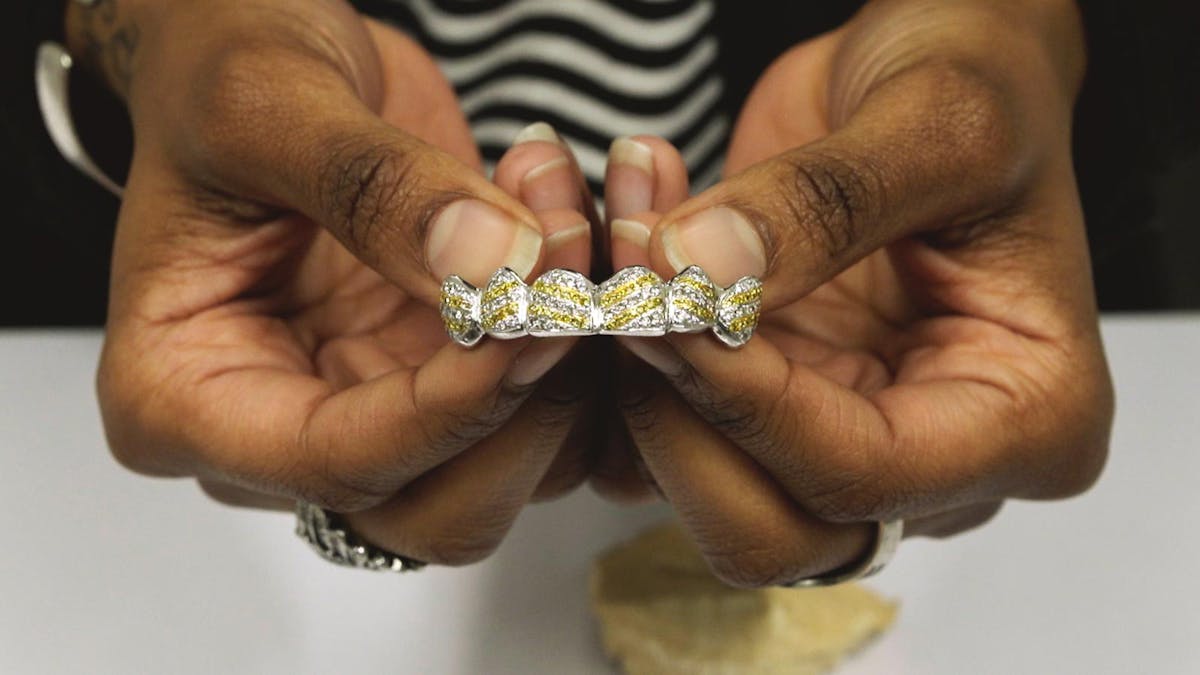 a pair of hands presenting a jewel encrusted grill for the mouth