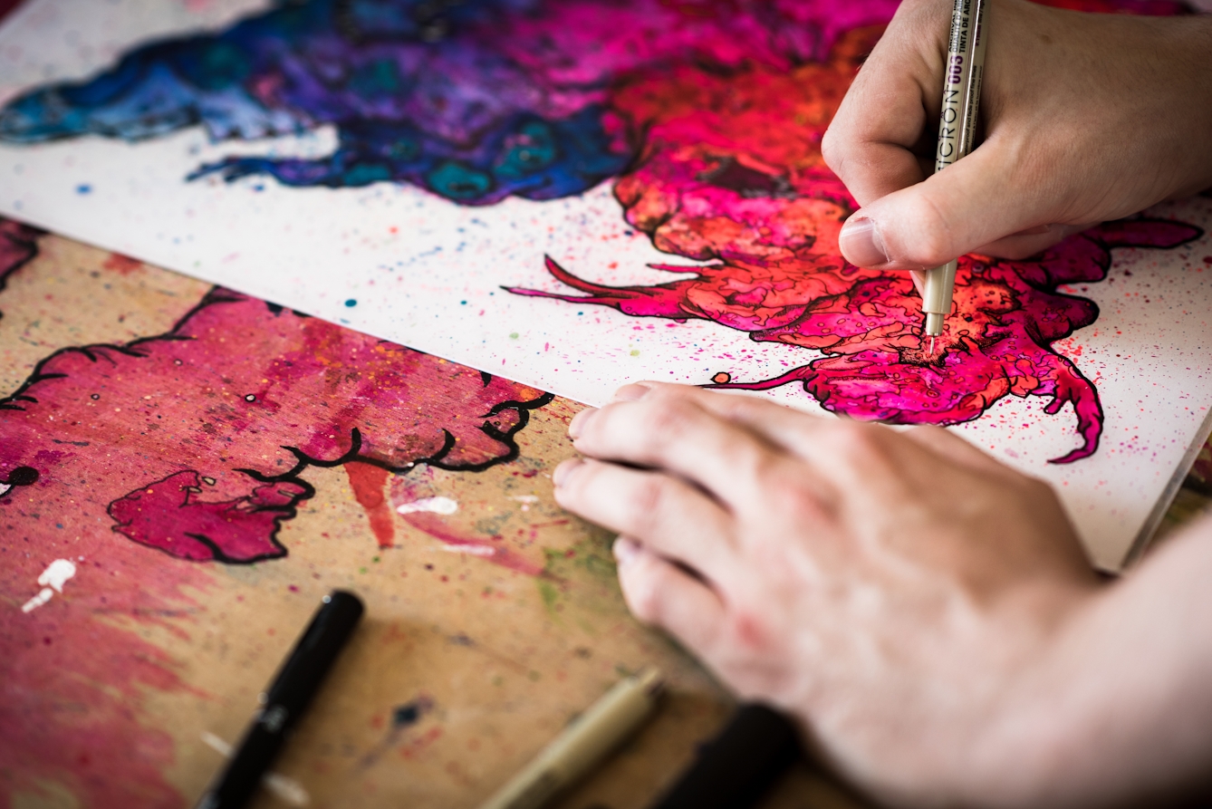 Photograph of a close up of a man's hand holding a pen which he is using to create a colourful artwork.