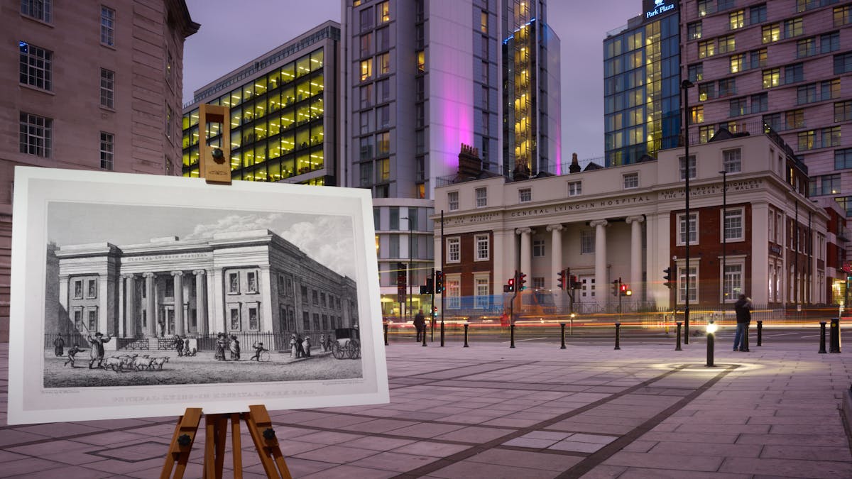 Photograph of the former General Lying-In Hospital with an historical image of the hospital displayed in front of it on a wooden artist's easel.