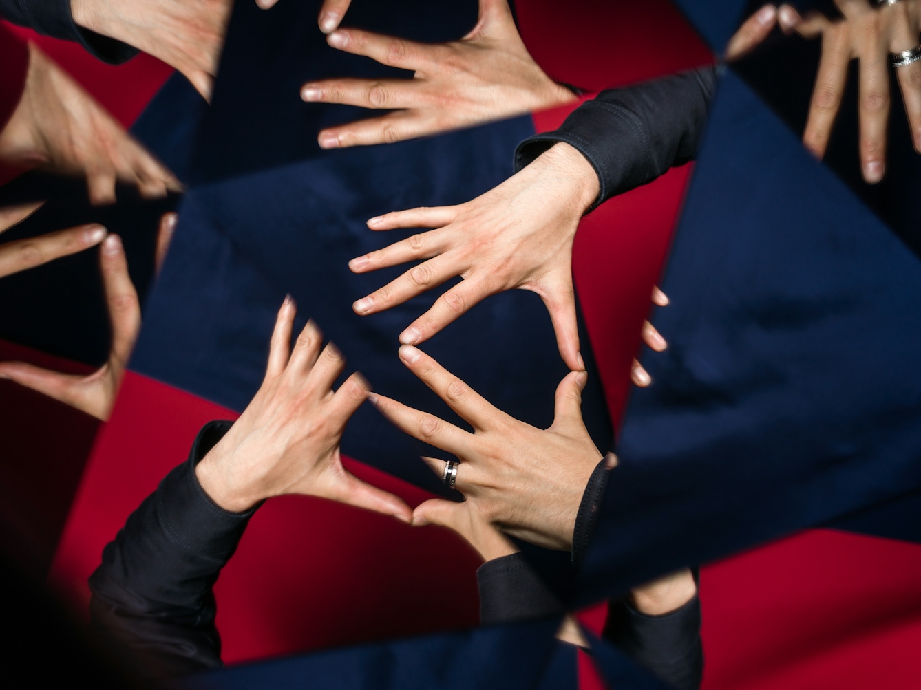 Photograph through a kaleidescope of hands with fingers outstretched. The background is made up of blue and red fabric.