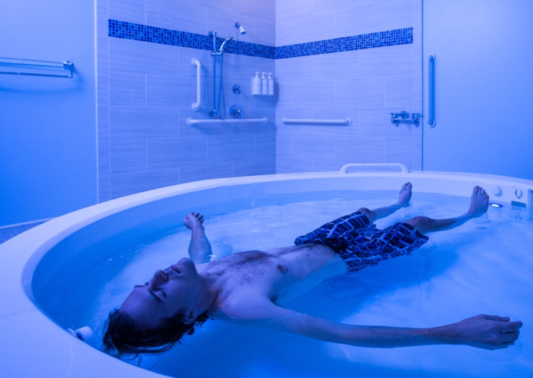 A man lies in a blue-lit pool of water.