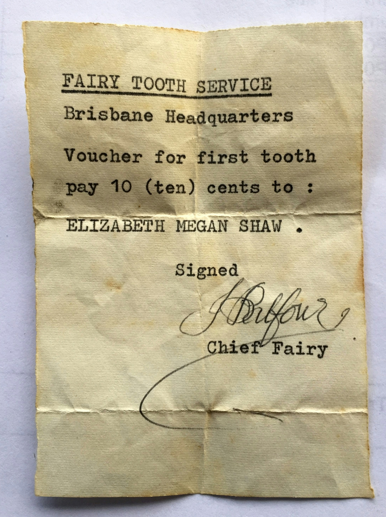 Letter typewritten in black ink on cream paper. Signed by hand in black ink with a flourish. Reads: FAIRY TOOTH SERVICE, Brisbane Headquarters. Voucher for first tooth, pay 10 (ten) cents to: ELIZABETH MEGAN SHAW. Signed J. Balfour, Chief Fairy. 