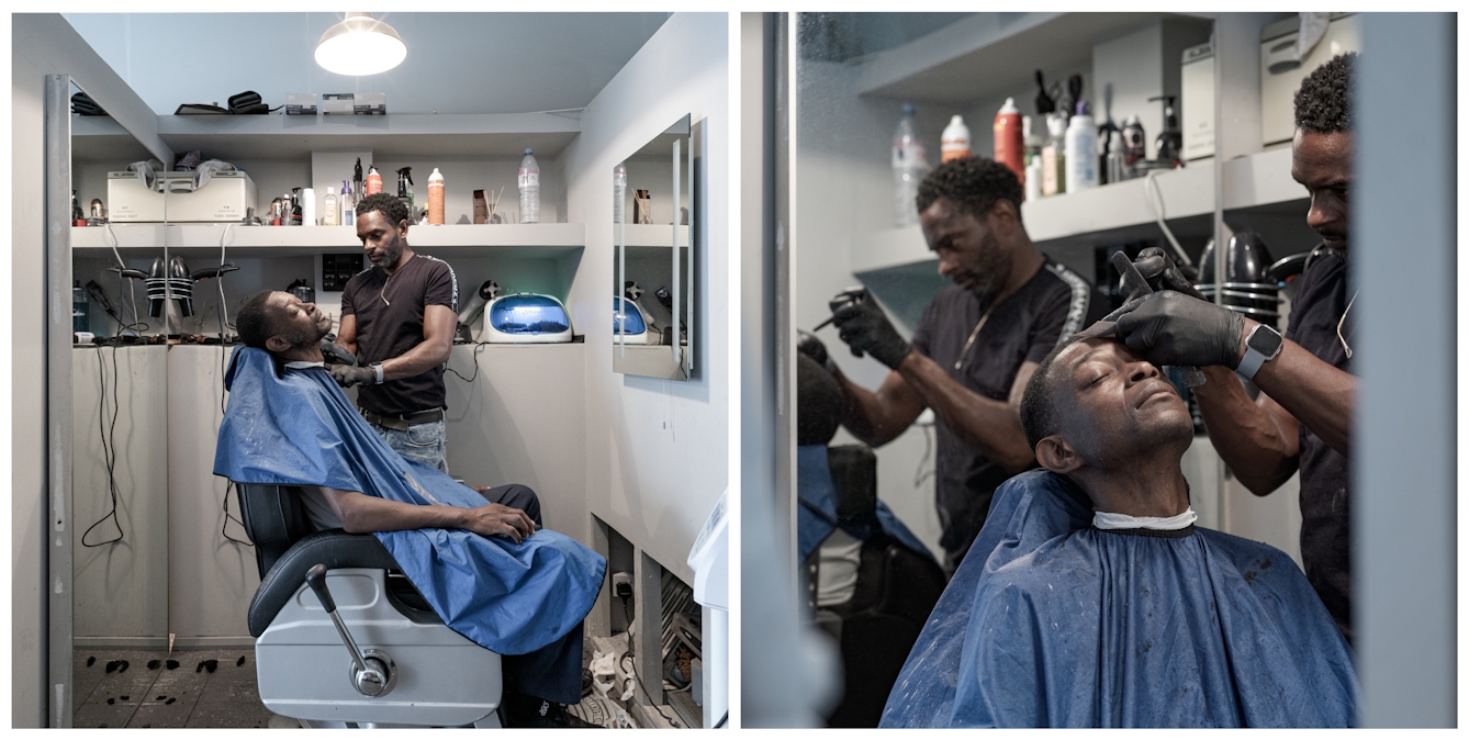 Photographic diptych. The photograph on the left shows a man from the side sitting in a barber's chair, draped in a blue hairdressing cape. Behind him the barber is cutting his hair. The photograph on the right show a closer view of the same man sitting in the same chair, with the barber to his left, concentrating hard on cutting his hair.