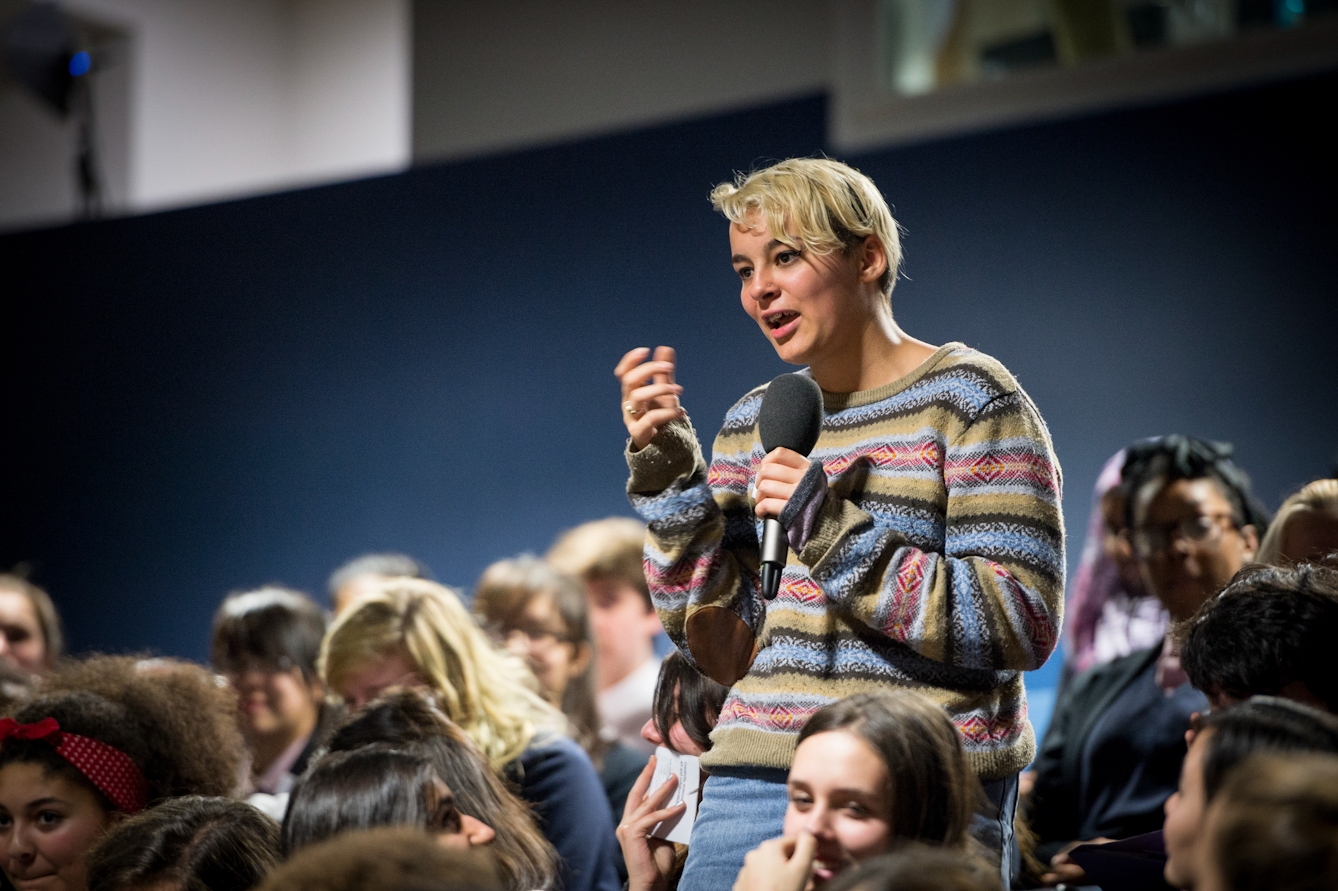Photograph of a young woman talking into a microphone at an event.