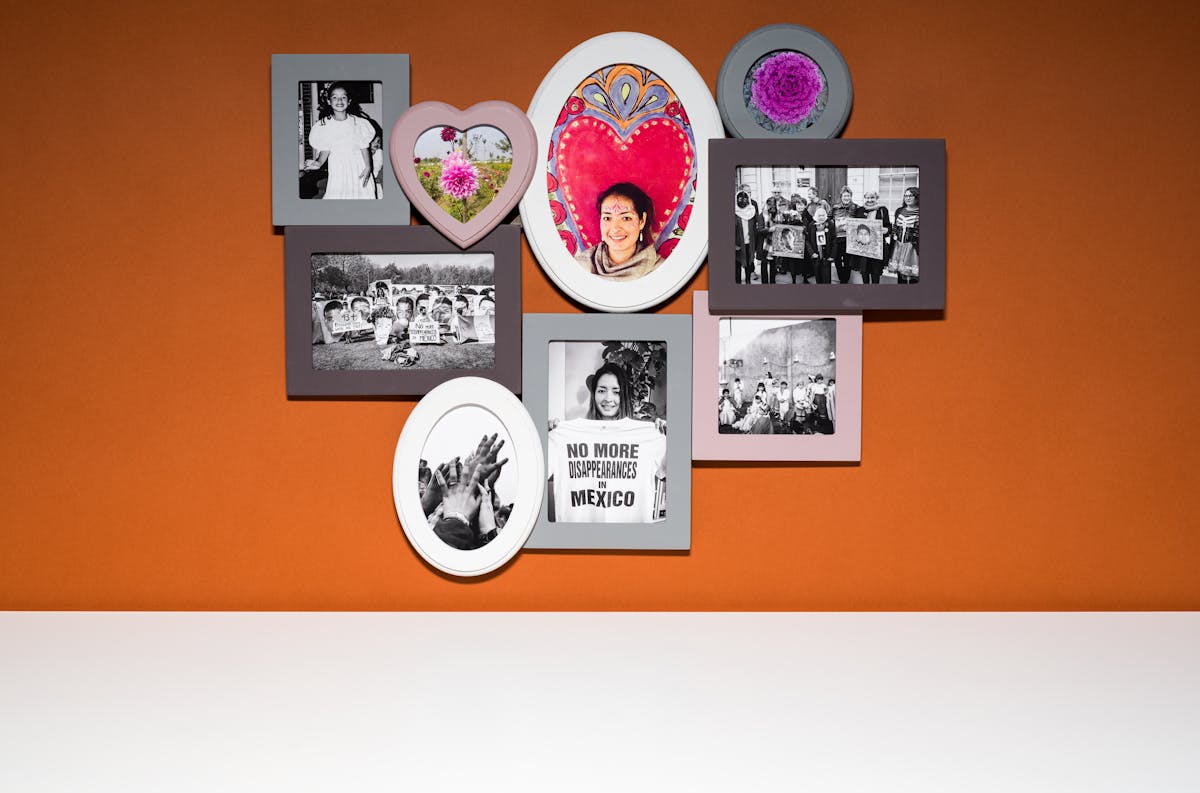 Photograph of a multiframe photo frame containing nine photographs, three in colour and six in black and white. The frame is hung on a brown wall above a white tabletop.