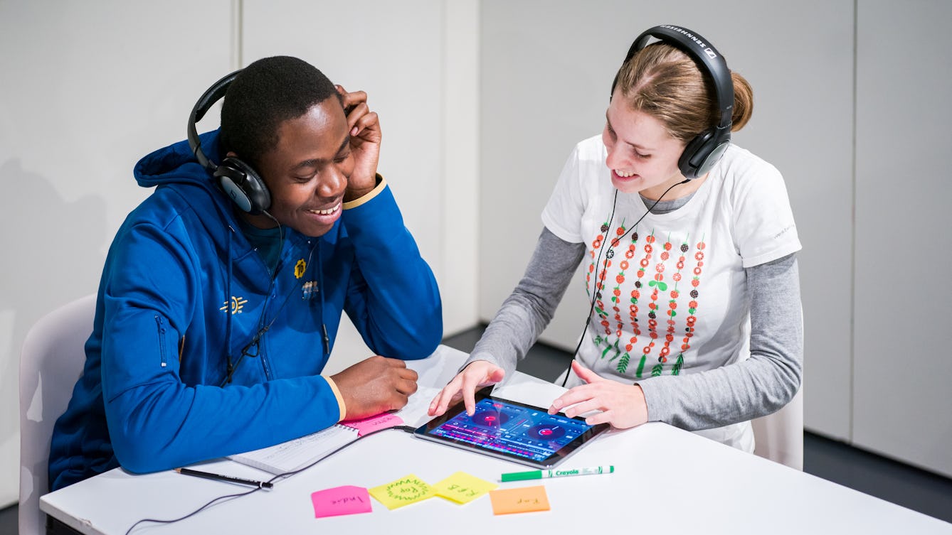 Photograph of a young woman and man sat at a table using a tablet device to create music as part of a Saturday Studio workshop at Wellcome Collection..