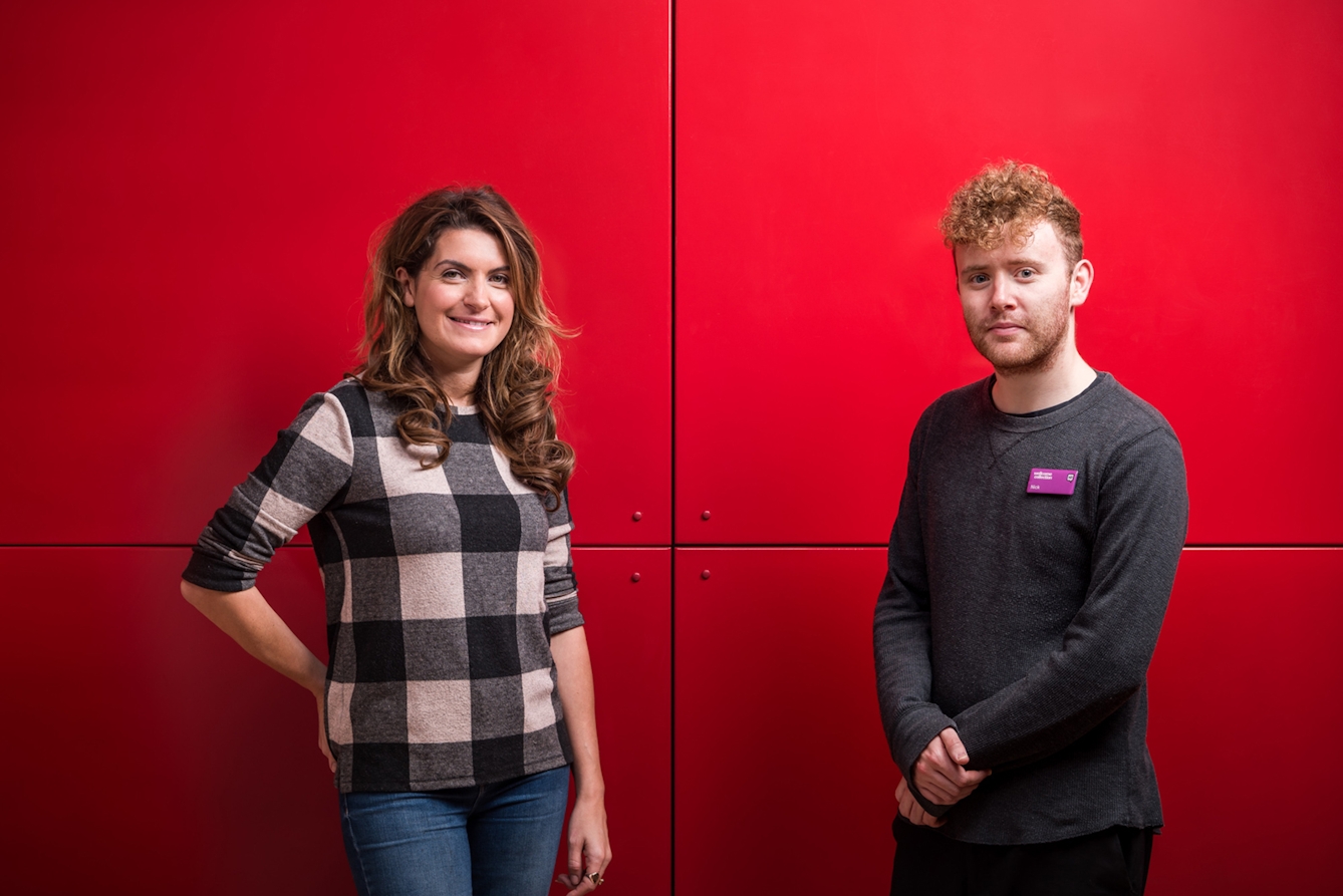 Portrait of a woman and a man standing against a bright red background