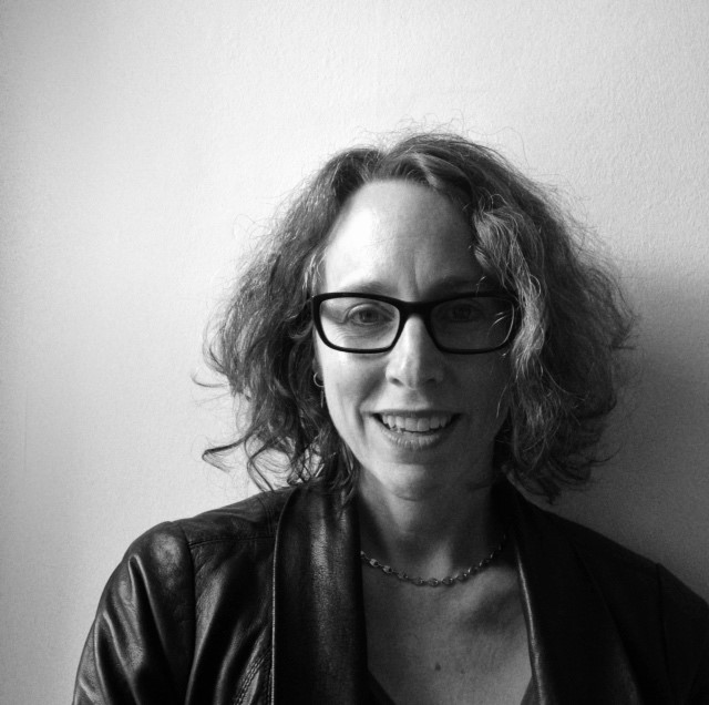 Portrait photograph of a woman with glasses and collar-length hair, smiling.