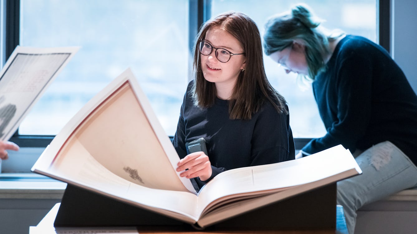 Photograph of a young women looking at a large facsimile book whilst researching in the Reading Room at Wellcome Collection.