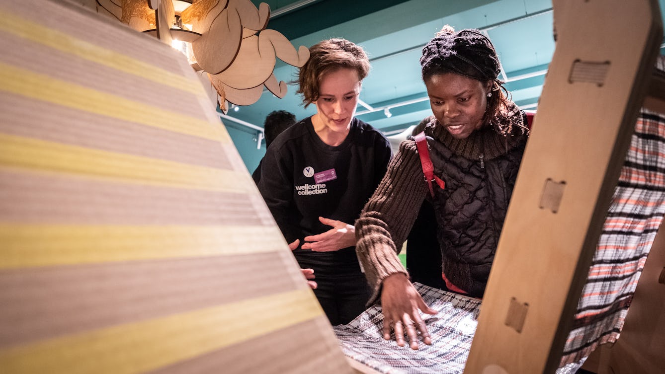 Photograph of a visitor experience assistant at Wellcome Collection giving an audio described tour to a woman who is blind or partially sighted.