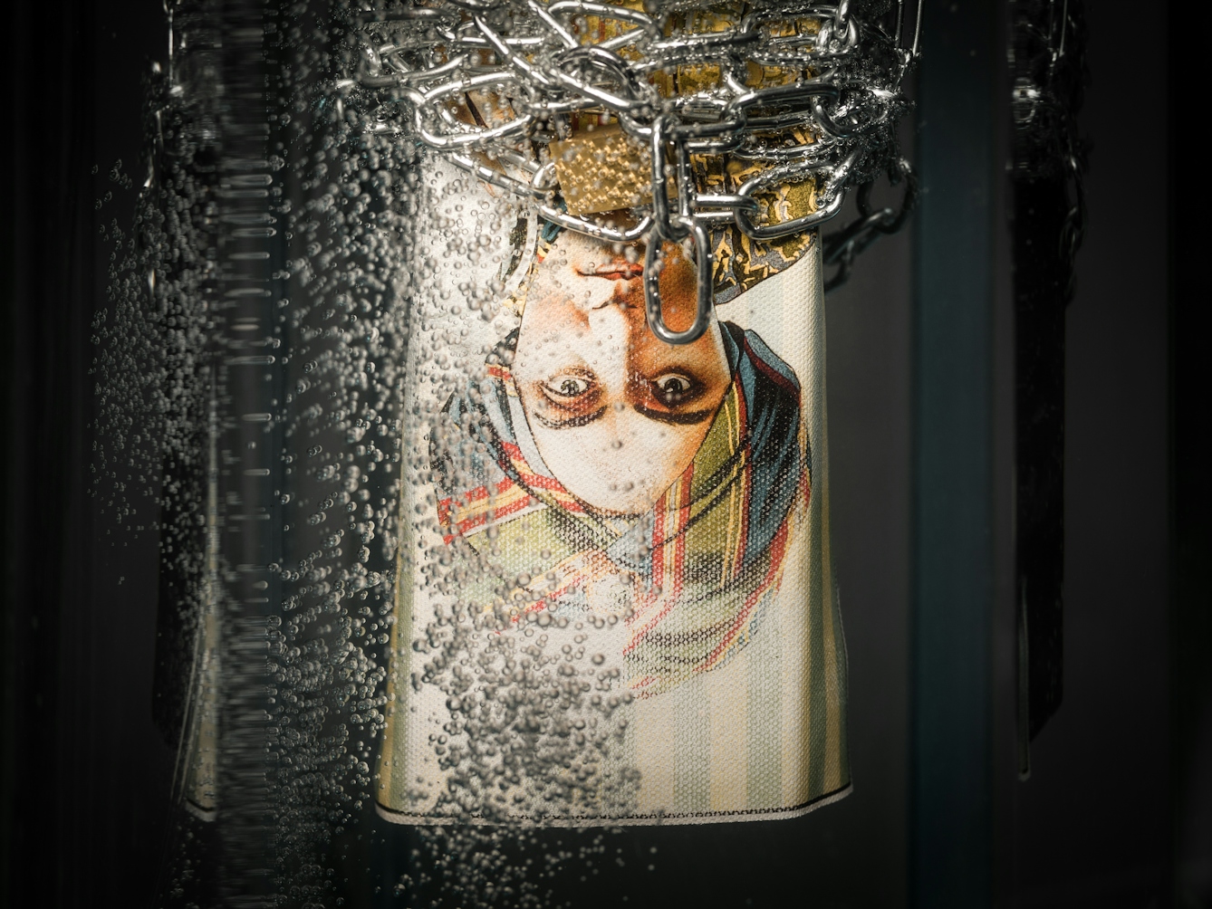 Photograph of a promotional poster for the 1920s mind reader, Alexander, hanging upside down in a tank of water wrapped in chains and padlocks, surrounded by bubbles.