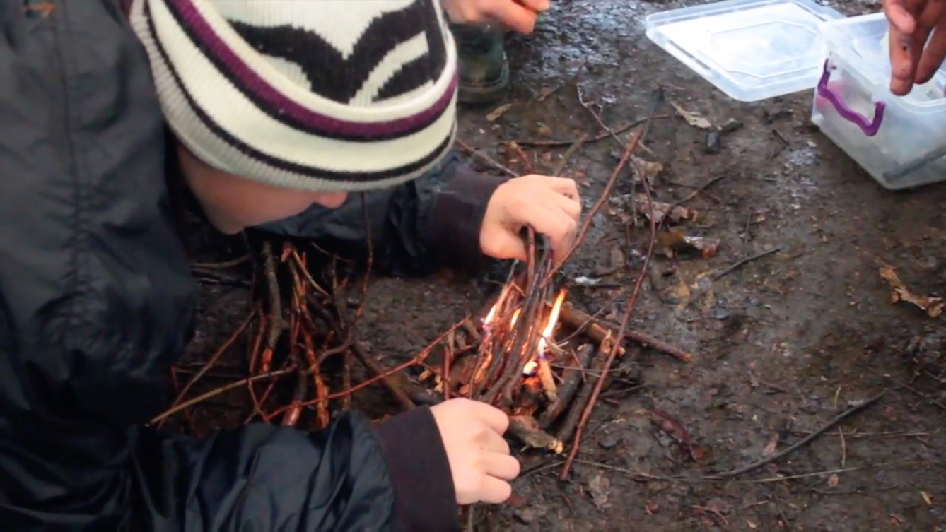 Film still showing a young boy lighting a fire in the woods, from 'Out of the Wild' a RawMinds film project.