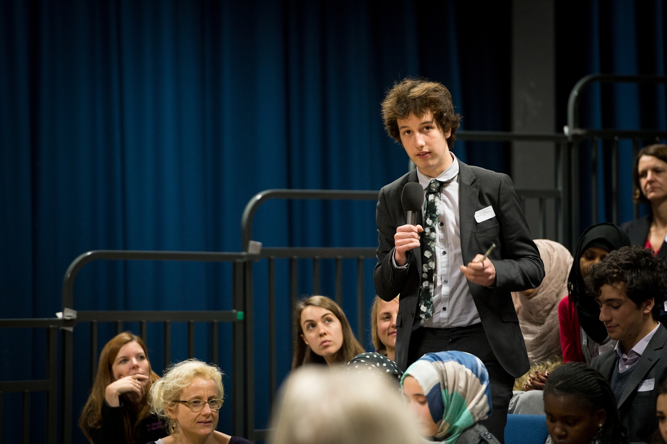 Photograph of a young man talking into a microphone at an event.