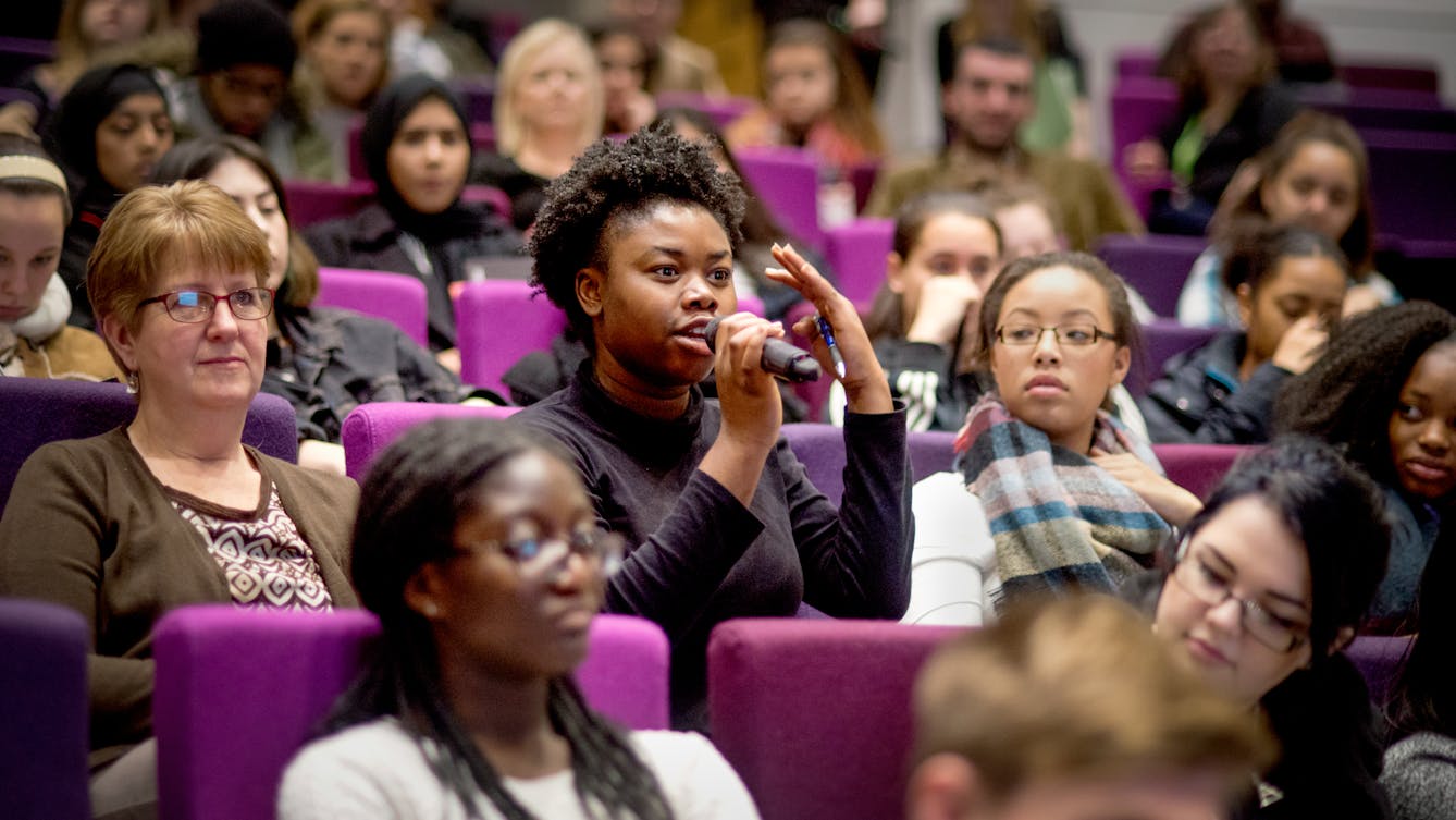 Photograph of the audience in the Henry Wellcome Auditorium, showing a young woman speaking into a microphone.