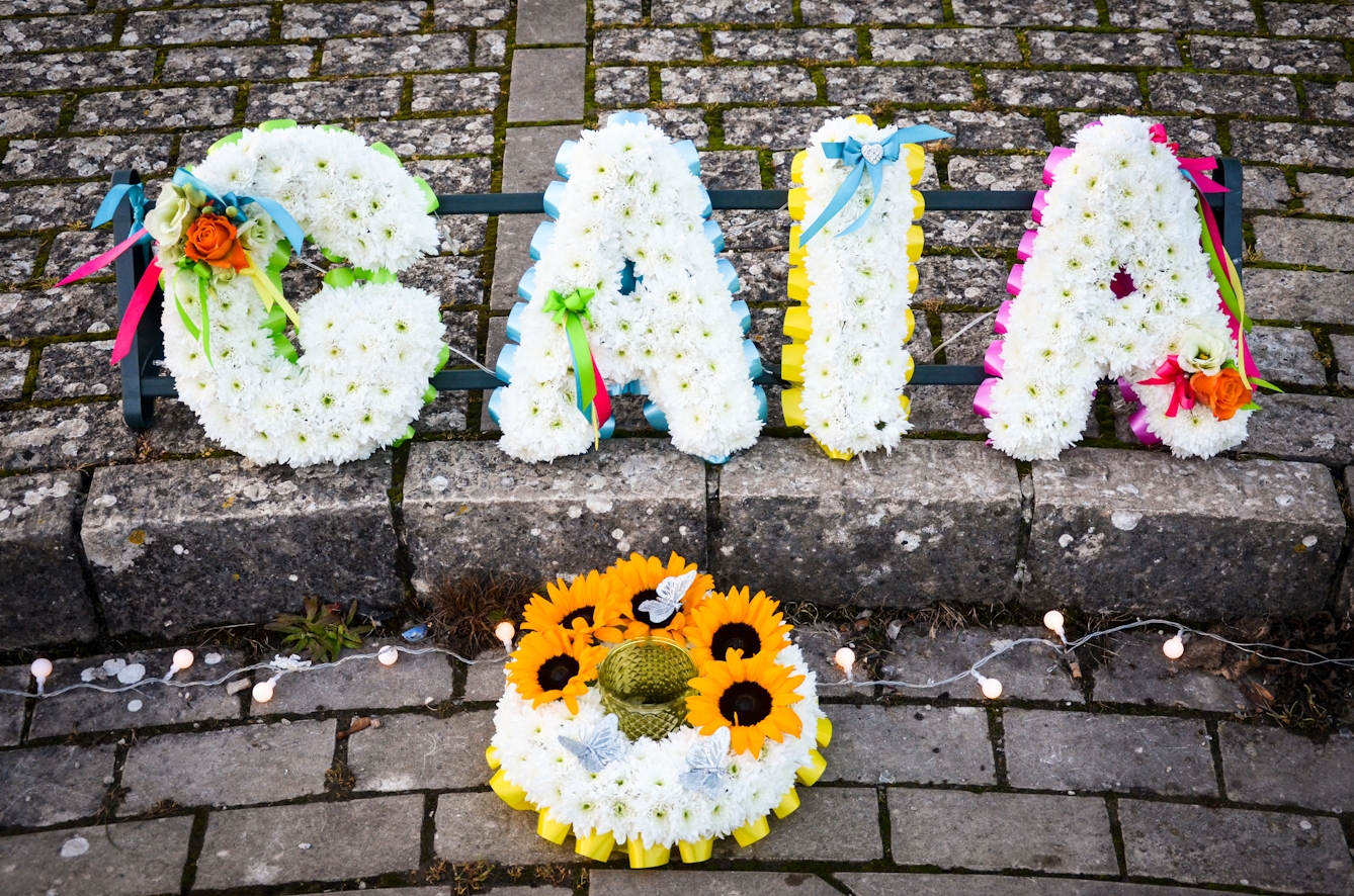 Photograph of flowers arranged into letters to spell the name Gaia, resting on brick paving.