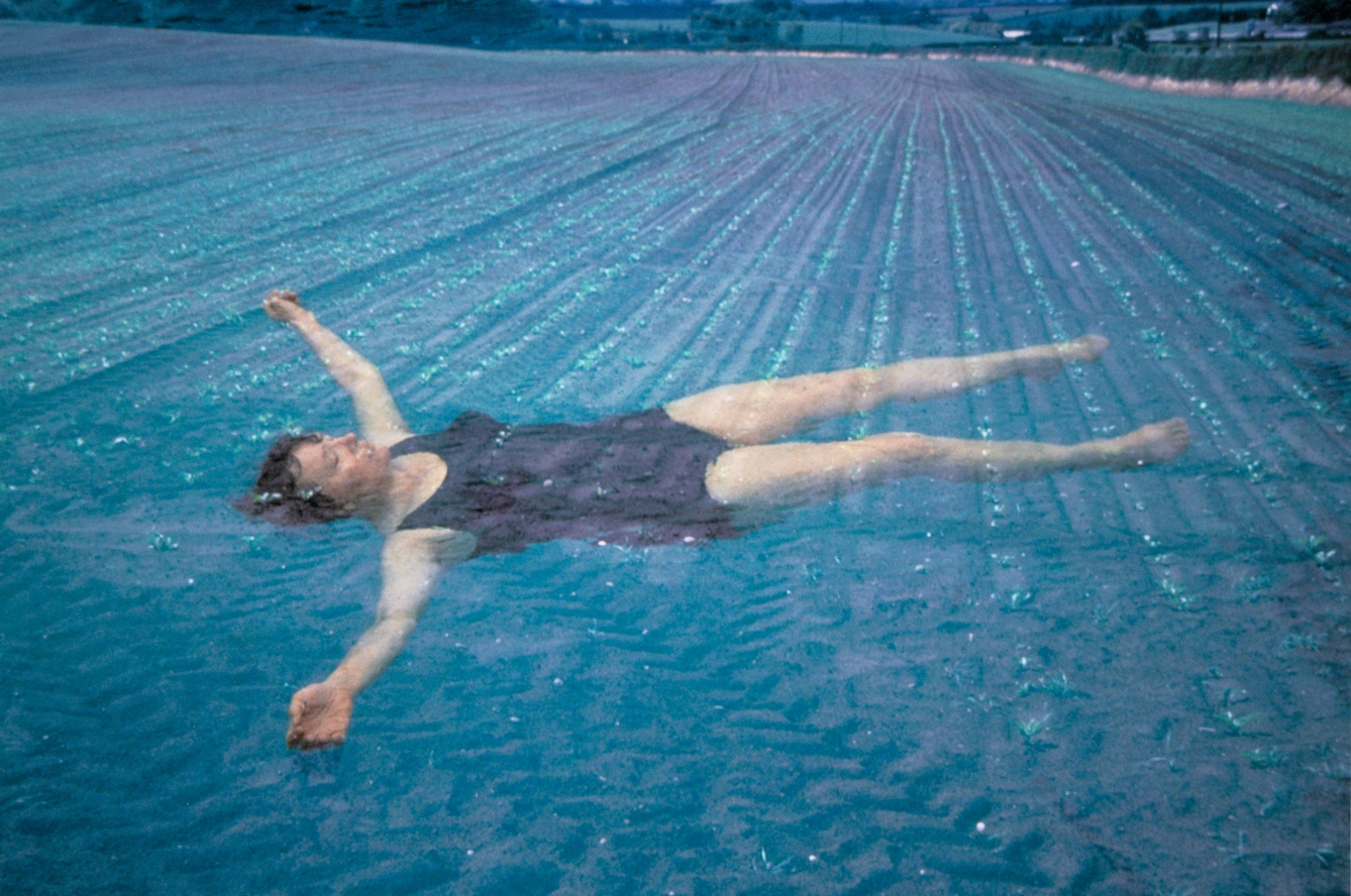 Photograph a woman in a swimming costume floating in water, superimposed on an image of an agricultural field.