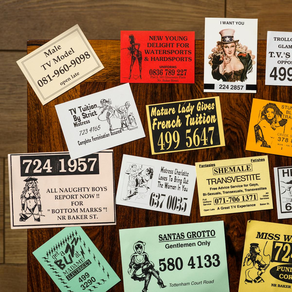 Photograph of a selection of cards from the sex worker card collection at Wellcome Collection, laid out on a wooden tabletop.