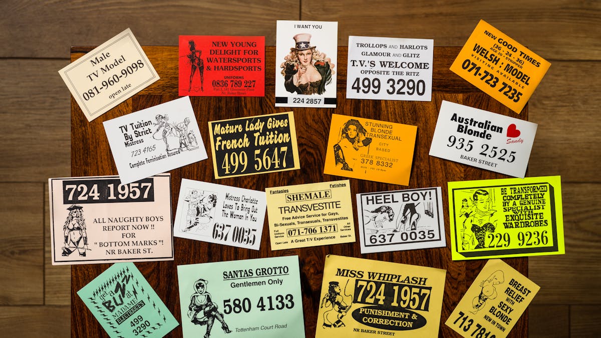 Photograph of a selection of cards from the sex worker card collection at Wellcome Collection, laid out on a wooden tabletop.