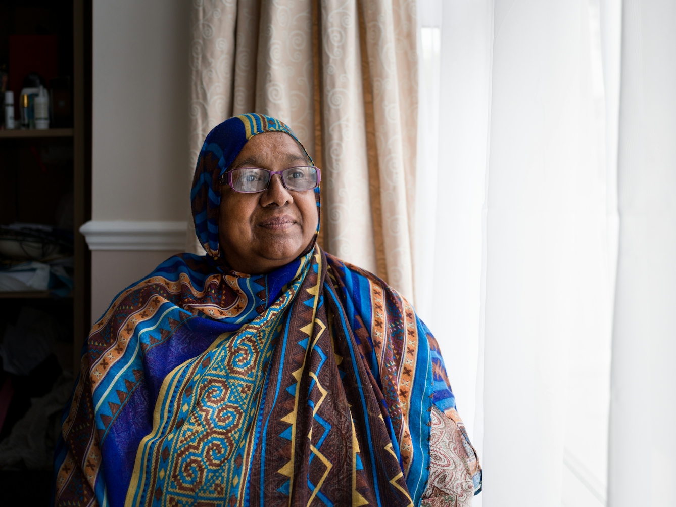 Photographic portrait of Sarifa Patel sitting next to the window in her living room.