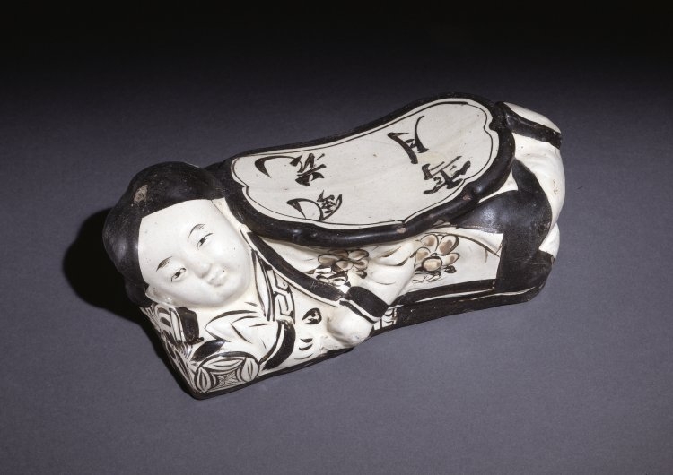Colour photograph of a black and white ceramic pillow in the shape of a woman reclining. 