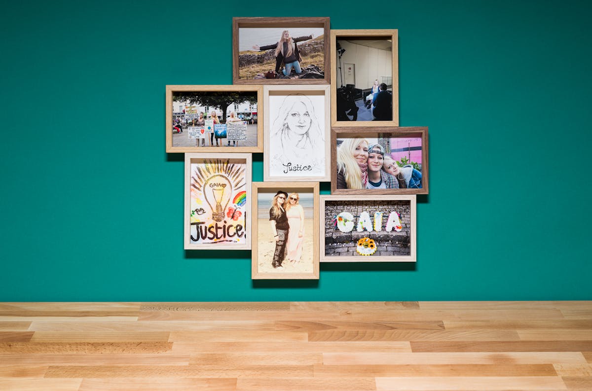 Photograph of a multiframe photo frame containing eight photographs, seven in colour and one in black and white. The frame is hung on a cyan-coloured wall above a wood block tabletop.